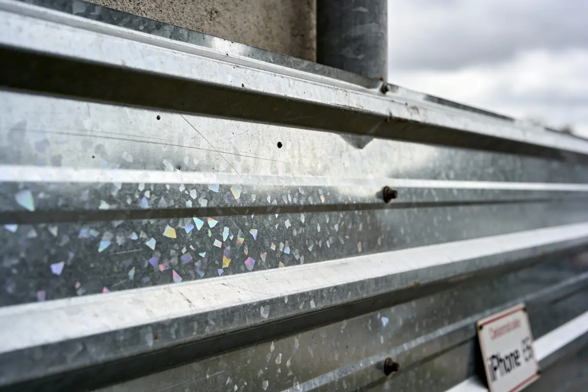 Plan rapproché de tôle en métal, fixée avec vis, surface réfléchissant des éclats colorés, sous ciel nuageux.