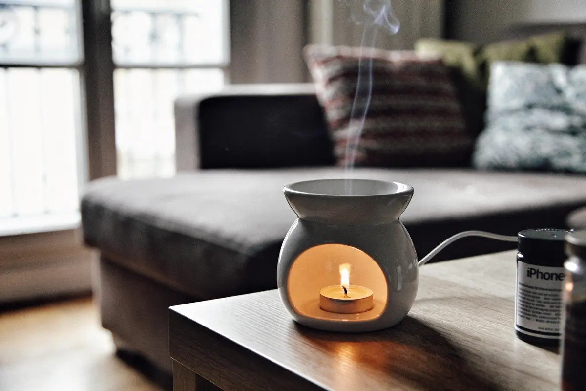 Bougie allumée dans un photophore, posée sur une table en bois, près d'un canapé et fenêtres.