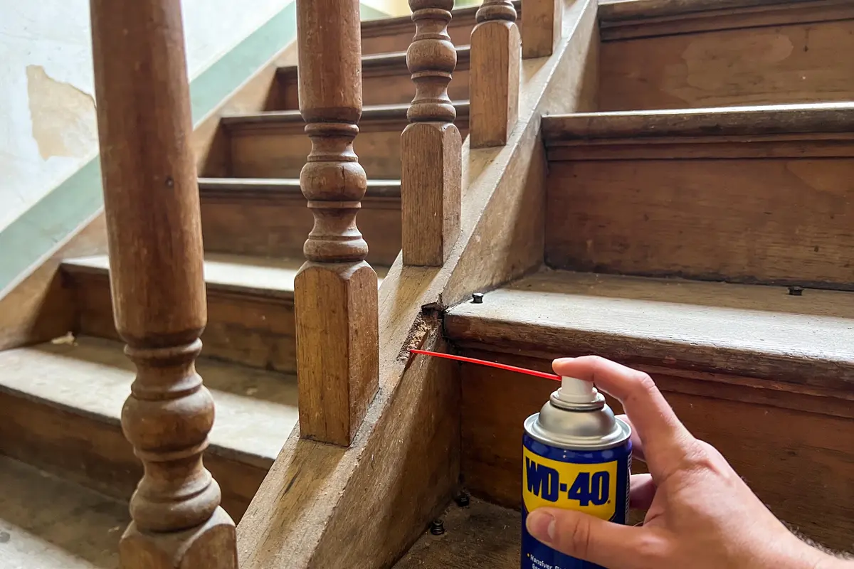 Main appliquant WD-40 sur escalier en bois pour entretien et réduction du bruit.