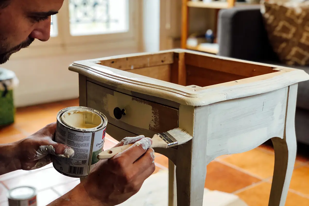 Homme peignant une table en bois avec un pinceau et de la peinture claire.